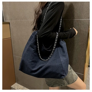 Detailed view of the large denim tote bag with silver chain strap worn by a model