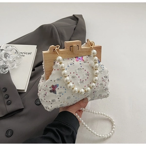 Detail of white denim shell bag featuring sequin butterfly embroidery and wood frame closure