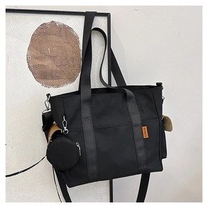 Detail view of black canvas tote bag with wide shoulder strap and round coin purse accessory