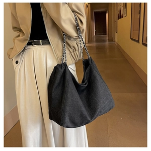 Detail of black denim tote bag with silver chain strap worn by a model in soft lighting