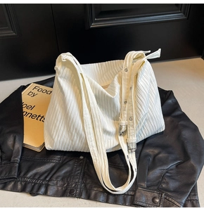 Detail der weißen Plissee-Tasche mit verstellbarem Ösenriemen auf Leder-Hintergrund