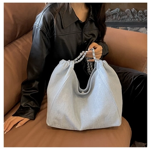 Close-up of light blue denim tote bag with silver chain strap on a brown sofa