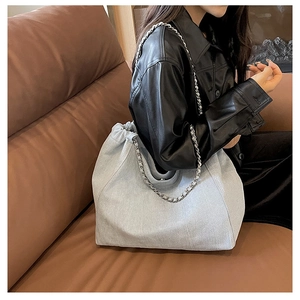 Close-up of light gray denim tote with pleated texture and stylish metal chain strap