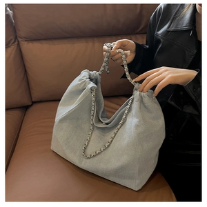 Detail of light blue denim hobo bag with drawstring opening and woven chain strap