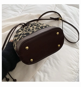 Detail view of leopard bucket bag with gold metal feet and premium brown leather base