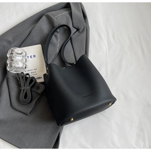 Détail du sac seau en cuir grainé noir avec clous dorés posé sur un blazer gris chic