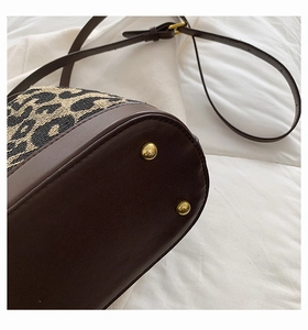 Detailed close-up of leopard print bucket bag with dark brown leather base and gold metal studs