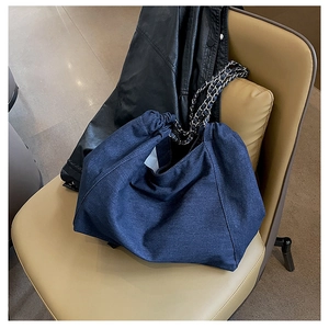 Detail of blue denim tote bag with silver chain strap on a brown leather chair