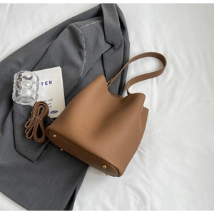 Détail du sac seau en cuir grainé marron avec des pieds en métal doré sur le dessous
