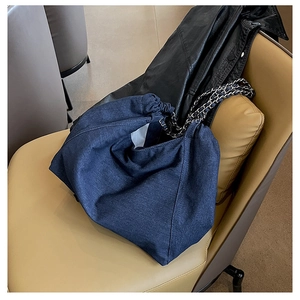 Detailed view of blue denim tote bag with silver metal chain strap on leather chair