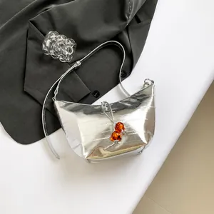 Detalle del bolso metalizado plateado con cuentas naranjas sobre tela de traje gris