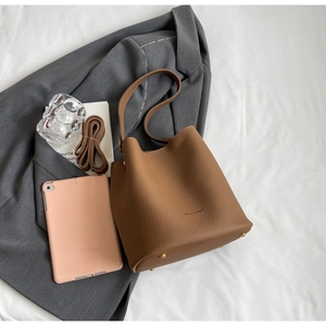 Détail du sac seau marron à motif litchi avec pieds de protection dorés sur un blazer