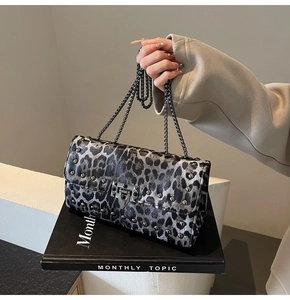 Sac bandoulière léopard avec chaîne noire et rivets posé sur un livre d'art