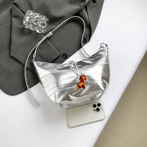 Detalle de bolso de hombro plateado grabado en cocodrilo con adorno de cuentas naranja