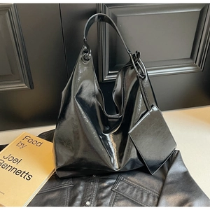 Detail of glossy black leather tote bag featuring a matching pouch and subtle texture