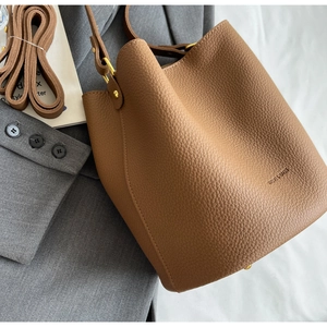 Détail d'un sac seau marron avec motif litchi, boucle dorée et bandoulière réglable