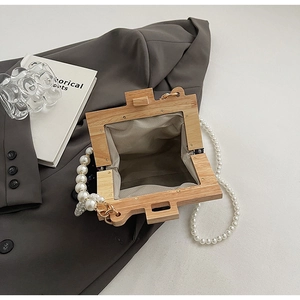 Detail of a square wooden frame handbag featuring large pearl handle and beige lining