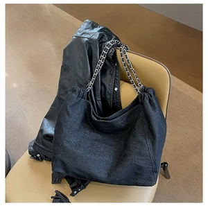 Detail of black denim tote bag with silver chain strap on a yellow chair in urban setting