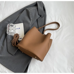 Détail du sac seau en cuir marron avec texture litchi et pieds en métal doré