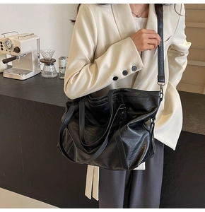 Detail of vintage black PU leather tote bag with dual straps held by model in beige suit