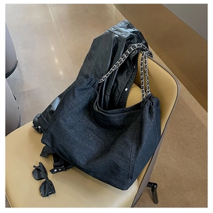 Detail of black denim tote bag with chain strap and drawstring on a leather seat