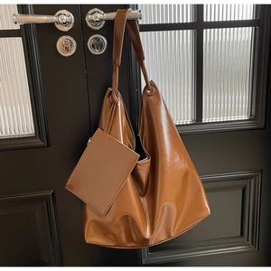 Detail of caramel leather hobo bag with matching pouch hanging on a dark wooden door