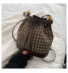 Detailed close-up of brown houndstooth drawstring bucket bag with leather base and gold buckle