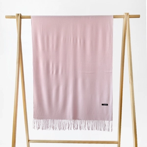 Solid soft pink cashmere scarf with tassels hanging on a minimalist wooden frame stand