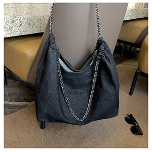 Macro detail of black denim tote bag featuring silver chain strap and drawstring design
