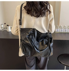 Detail view of a black PU leather tote bag worn as a shoulder bag on a female model