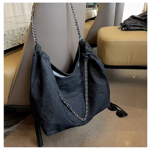 Detail of black denim hobo bag featuring a silver metal chain strap and pleated opening