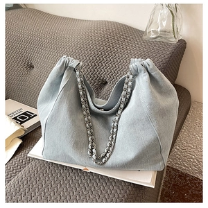 Close-up of light blue denim tote bag with elegant chain straps on a grey sofa