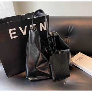 Detail view of glossy black tote bag with褶皱 texture and matching mini pouch on a sofa
