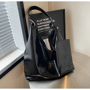 Detail of high-gloss black hobo bag with matching small pouch on a metal table