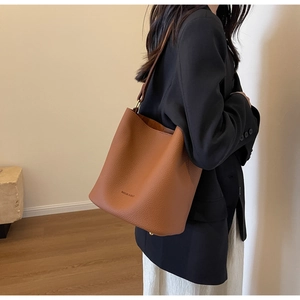 Sac seau marron caramel avec texture litchi porté à l'épaule dans un décor moderne
