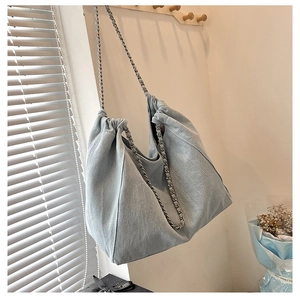 Detailed view of large denim tote bag with elegant silver chain strap and pleated texture