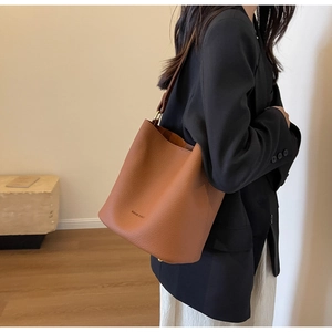 Sac seau en cuir grainé marron porté à l'épaule par un mannequin dans un salon