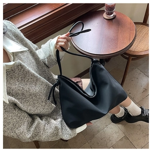 Détail d'un grand sac hobo noir avec nœud latéral dans un décor de café élégant