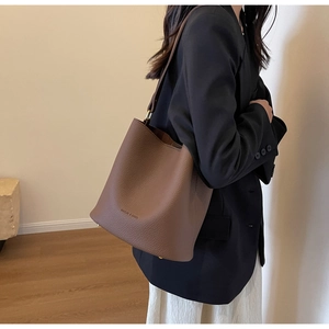 Grand sac seau en cuir marron avec large bandoulière porté sur un blazer noir