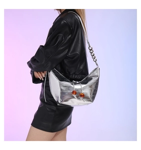 Detalle de bolso medialuna plateado con textura metálica y cuentas ámbar
