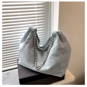 Detail of light blue denim tote with drawstring closure and metal chain strap on gift box