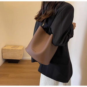 Détail du sac seau en cuir marron foncé avec motif litchi, logo de marque et bandoulière