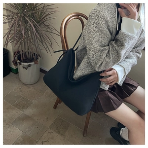 Sac à bandoulière hobo noir classique porté avec une tenue élégante en tweed gris chez soi