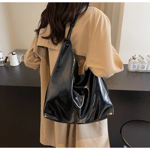 Model wearing a high-gloss black leather hobo bag with a minimalist shoulder strap