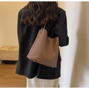 Détails d'un sac seau en cuir marron avec clous dorés porté par un mannequin de dos