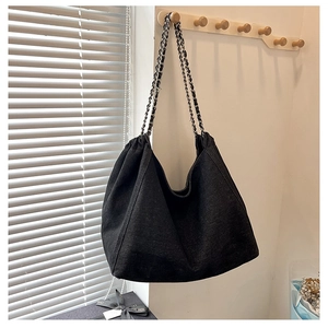 Close-up of black denim tote bag with elegant chain strap hanging on wooden wall hook