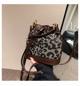 Detail view of leopard print canvas bucket bag with brown leather trim and gold hardware