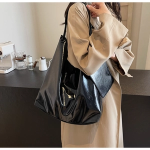 Close-up of a large black glossy patent leather hobo bag worn with a casual trench coat