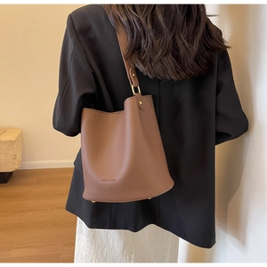 Détail du sac seau en cuir grainé marron foncé avec large bandoulière et métal doré