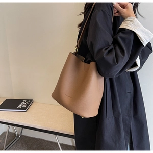 Détail d'un sac seau en cuir marron grainé avec connecteurs de bandoulière métalliques chic